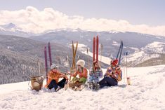 four skiers sitting in the snow on top of a mountain with their skis