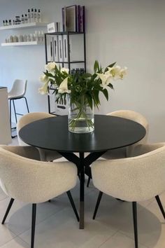 a black table with four chairs and a vase filled with flowers on top of it