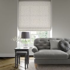 a living room scene with focus on the grey couch and window blinds in the background