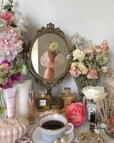 a cup of coffee sitting on top of a table next to a mirror and flowers