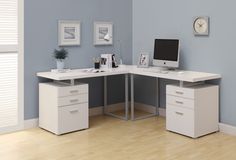 an office desk with two drawers and a computer monitor on top of it, in front of a blue wall