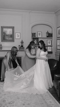 two bridesmaids helping the bride put on her wedding dress in black and white