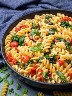 a bowl filled with pasta and spinach on top of a blue cloth next to tomatoes