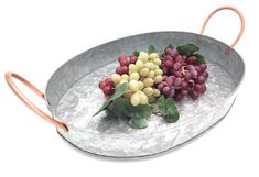 some grapes are in a metal bowl with leaves on the rim and one is red