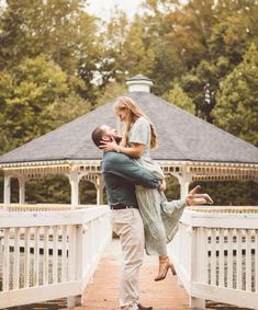 a man holding a woman in his arms as they stand on a bridge near a gazebo