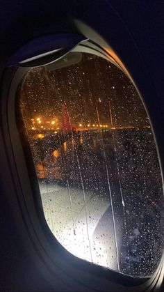 an airplane window with rain drops on the glass and city lights in the back ground