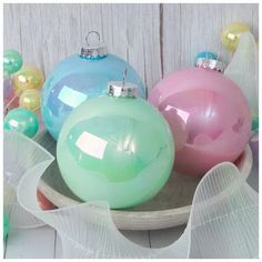 three different colored ornaments on a plate with white ribbon around the edge and one is pink, blue, green and yellow