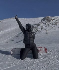 a snowboarder sitting on the ground with his arms in the air and one hand up