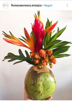 a person holding a vase with flowers in it and palm fronds on the inside