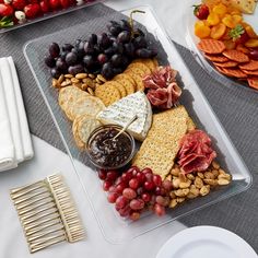 a platter filled with grapes, crackers, cheese and meats next to other snacks