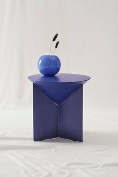 a blue vase sitting on top of a purple table with a black flower in it