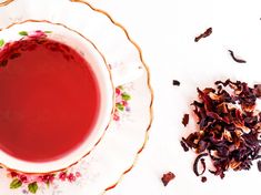 a tea cup and saucer filled with red liquid next to dried flowers on a white surface