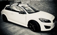 a white car parked in front of a brick wall with skis on the roof