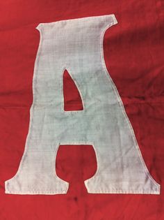 the letter a is made out of white fabric on a red cloth with a black outline