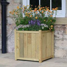 a wooden planter filled with lots of flowers next to a brick wall and window