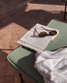 an open book with sunglasses on top of it sitting on a bench next to a table