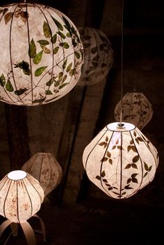 three hanging lamps with leaves on them in the dark, one is white and the other is green