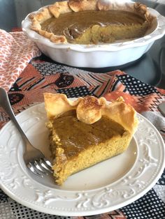 a slice of pumpkin pie on a plate with a fork next to the pie dish