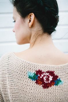 a woman is wearing a sweater with flowers on the back, and has her hair in a bun