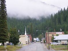 an empty street with cars parked on the side and fog hanging over the mountains in the distance