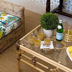 a glass table topped with drinks next to a wicker chair and footstool