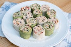 a white plate topped with rolls covered in spinach and other toppings on top of a wooden table