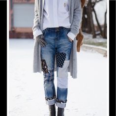 a woman standing in the snow wearing jeans and a cardigan jacket with patches on it