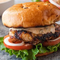 a chicken sandwich with lettuce, tomato and sauce on it sitting on a table