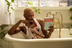 a man sitting in a bathtub reading a book next to a faucet