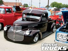 classic trucks are parked in a parking lot with other cars and people looking at them