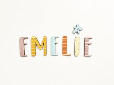 the word emelie spelled with colorful wooden letters on a white surface next to a flower