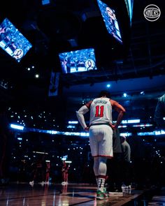 a basketball player stands on the court in front of several television screens and lights above him