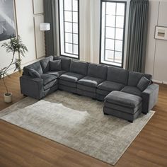 a large sectional couch in a living room with two windows and a rug on the floor