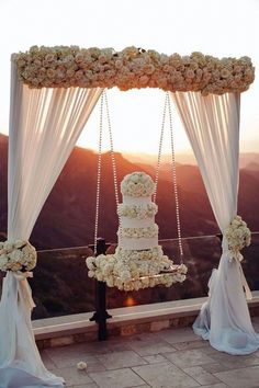 a wedding cake on top of a table covered in white flowers and hanging from the ceiling