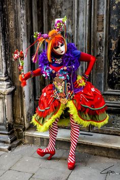 a woman dressed as a clown standing in front of a building with red and yellow hair