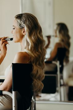 a woman is sitting in a chair while she brushes her long hair with a brush