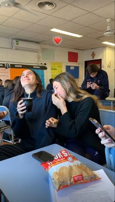 two women sitting at a table with their cell phones in front of them, laughing