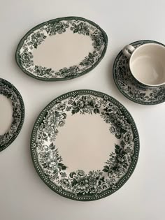 three plates with green and white designs on them, next to a cup and saucer