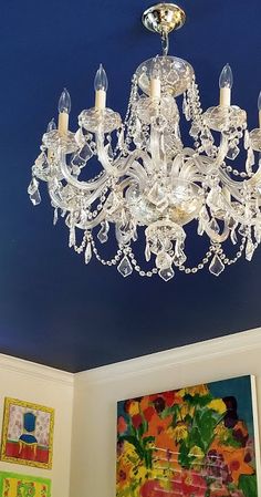 a chandelier hanging from the ceiling in a room with blue walls and paintings