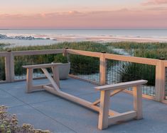 a wooden bench sitting on top of a cement patio next to the ocean at sunset