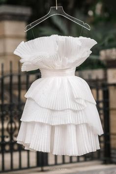 a white dress hanging on a black iron fence with a hanger in the foreground