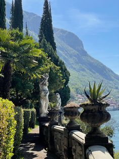 some statues are sitting on the side of a path near water and trees with mountains in the background