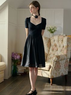 a woman in a black dress is standing near a chair