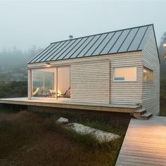 a small wooden house on the edge of a grassy field with a deck leading to it