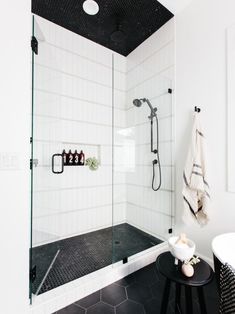 a black and white tiled bathroom with glass shower door, stools and towel rack