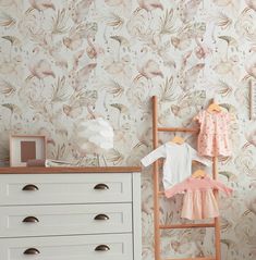 a baby's room with floral wallpaper and white dresser, pink dress on hanger