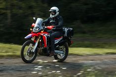 a man riding on the back of a red motorcycle down a dirt road with trees in the background