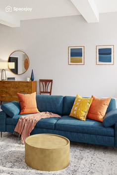 a living room with blue couches and orange pillows on the floor, in front of a mirror