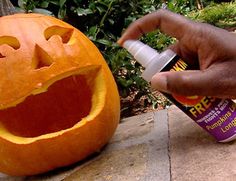 a person is carving a pumpkin with an orange face on it and holding a spray bottle in their hand