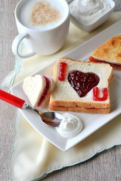 two pieces of toast with jam and cream on them next to a cup of coffee